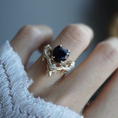 a woman's hand wearing a ring with a blue stone on it and leaves