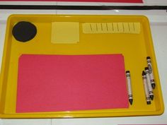 a yellow tray with pink paper and crayons on the bottom, along with two pens