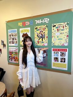 a young woman standing in front of a bulletin board with posters on the wall behind her