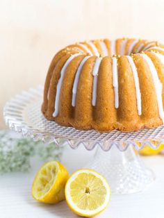 a bundt cake with icing and lemons on a glass platter next to two slices of lemon