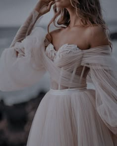 a woman in a white dress is standing near the ocean with her hands on her head