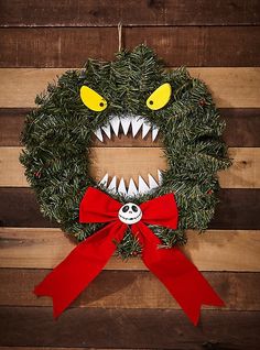 a wreath with a monster's mouth and red bow hanging on a wooden wall