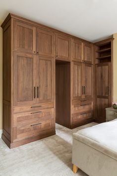 a bed sitting in a bedroom next to a wooden closet filled with drawers and cupboards