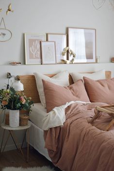 a bed with pink linens and pillows in a white room next to pictures on the wall