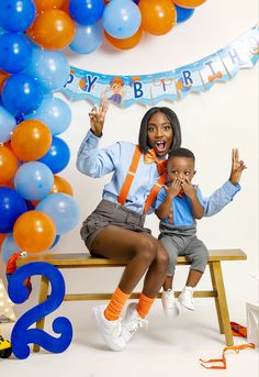 a woman and child sitting on a bench in front of balloons with the number two