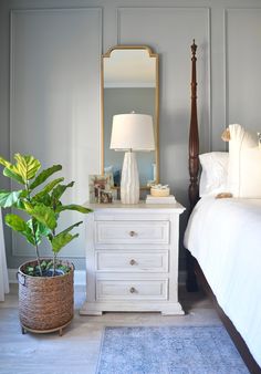 a white bed sitting next to a wooden dresser with a mirror on top of it