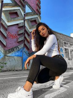 a beautiful young woman sitting on the ground in front of a wall with graffiti painted on it