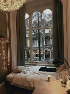 a bedroom with a large window and a bed in front of the window is lit by string lights