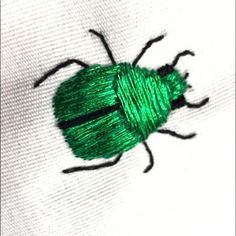 a close up of a green bug on a white shirt with black outline and thread