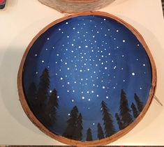 a painted wooden bowl sitting on top of a counter next to a plate with trees