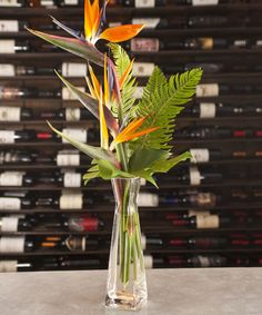 a vase filled with lots of flowers on top of a table next to wine bottles