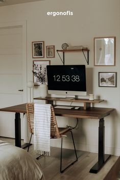 a desk with a computer on top of it next to a bed and pictures hanging on the wall