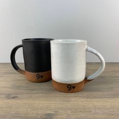 two black and white coffee mugs sitting side by side on a wooden table top