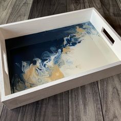 a white and blue painting in a wooden box on the floor with wood planks