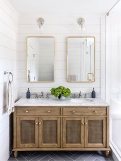 a bathroom with two mirrors above the sinks and a wooden cabinet below it, along with white walls