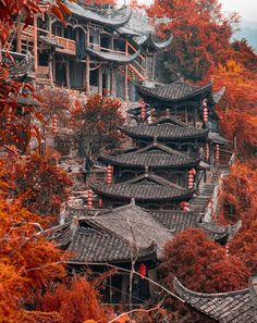 an old chinese village in autumn with red leaves on the trees and mountains behind it