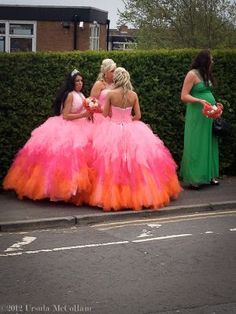 three women in dresses are standing on the side of the road, one is wearing a pink and orange dress