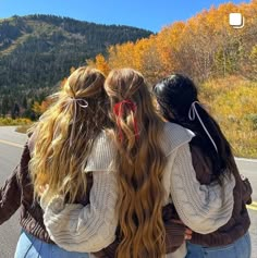 three girls are standing on the side of the road with their arms around each other