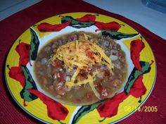 a yellow and red plate topped with chili and beans covered in cheese on top of it