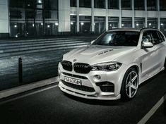 a white bmw suv parked on the side of a road at night in front of a building