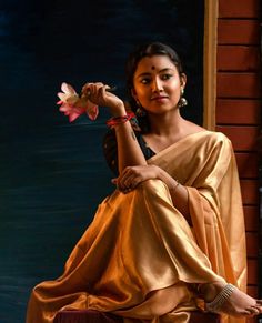 a woman sitting on top of a chair holding a flower in her right hand and looking at the camera