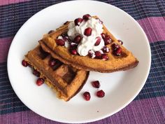 two waffles topped with whipped cream and pomegranate on a white plate