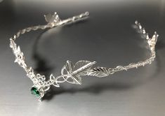 a close up of a silver bracelet with leaves and green stones on the clasps