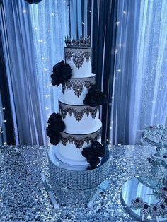 a three tiered wedding cake with black flowers on the top and silver sequins