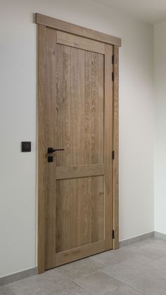 an empty room with a wooden door and tile flooring on the ground, in front of a white wall