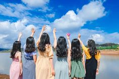 four girls are standing by the water and reaching for something in the sky with their hands