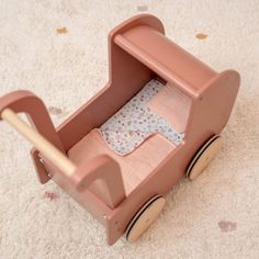 a pink toy car with a wooden handle on the floor next to a white carpet