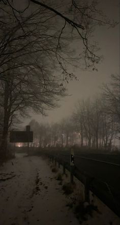 a snowy path with trees and street lights in the distance, at night on a foggy day