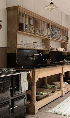 an old fashioned kitchen with black counters and wooden shelves, dishes on the stove top