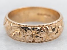 a gold wedding band with flowers and leaves engraved on the side, set in 18k yellow gold