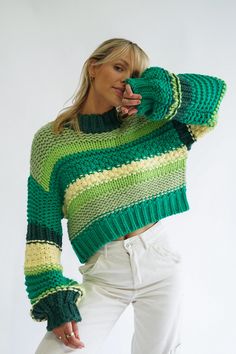 a woman wearing a green and yellow striped sweater with her hands on her face while standing in front of a white background