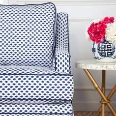 a blue and white patterned chair next to a small table with flowers in it on top