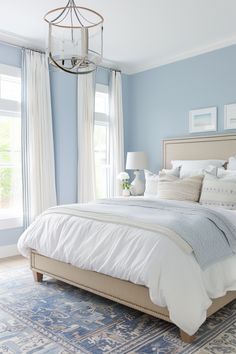 a bedroom with blue walls, white bedding and a chandelier hanging from the ceiling