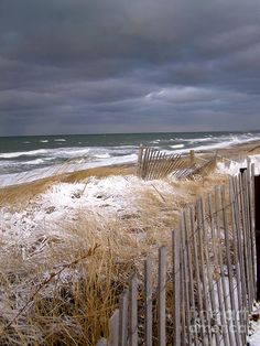 the beach is covered in snow and grass as storm clouds loom over the ocean