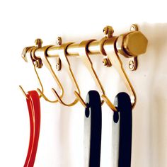 three pairs of scissors hanging from hooks on a white wall next to each other with red and black handles