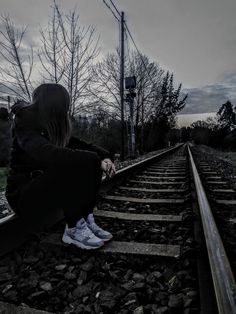 a woman sitting on train tracks looking at the sky