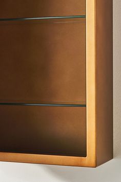 a wooden cabinet with three glass shelves on the front and bottom, against a white wall