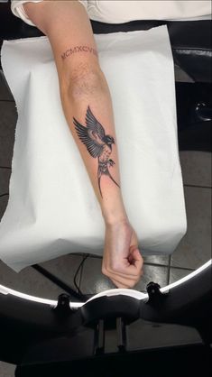 a person with a bird tattoo on their arm is sitting on a chair and holding onto a pillow