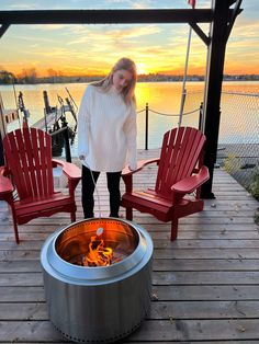 a woman standing next to two red chairs near a fire pit on a wooden deck