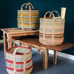 three baskets sitting on top of a wooden bench next to a blue wall with a roll of toilet paper in it