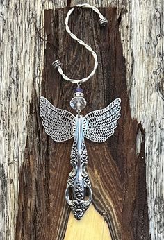 a necklace with an angel design on it hanging from a piece of wood, against a wooden background