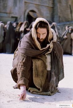 a man kneeling on the ground with his hands in his pockets and wearing a hooded jacket