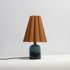 a blue table lamp sitting on top of a white bed next to a brown shade