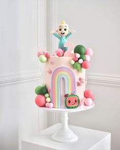 there is a pink cake with a rainbow decoration on the top and a small monkey on top