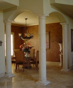 an archway leads to the dining room and formal living area in this home, with marble flooring and white columns