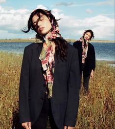 two people standing in tall grass near the water and one is wearing a scarf over her head